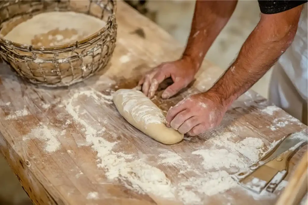 Hands shaping sourdough dough into a baguette on a floured surface